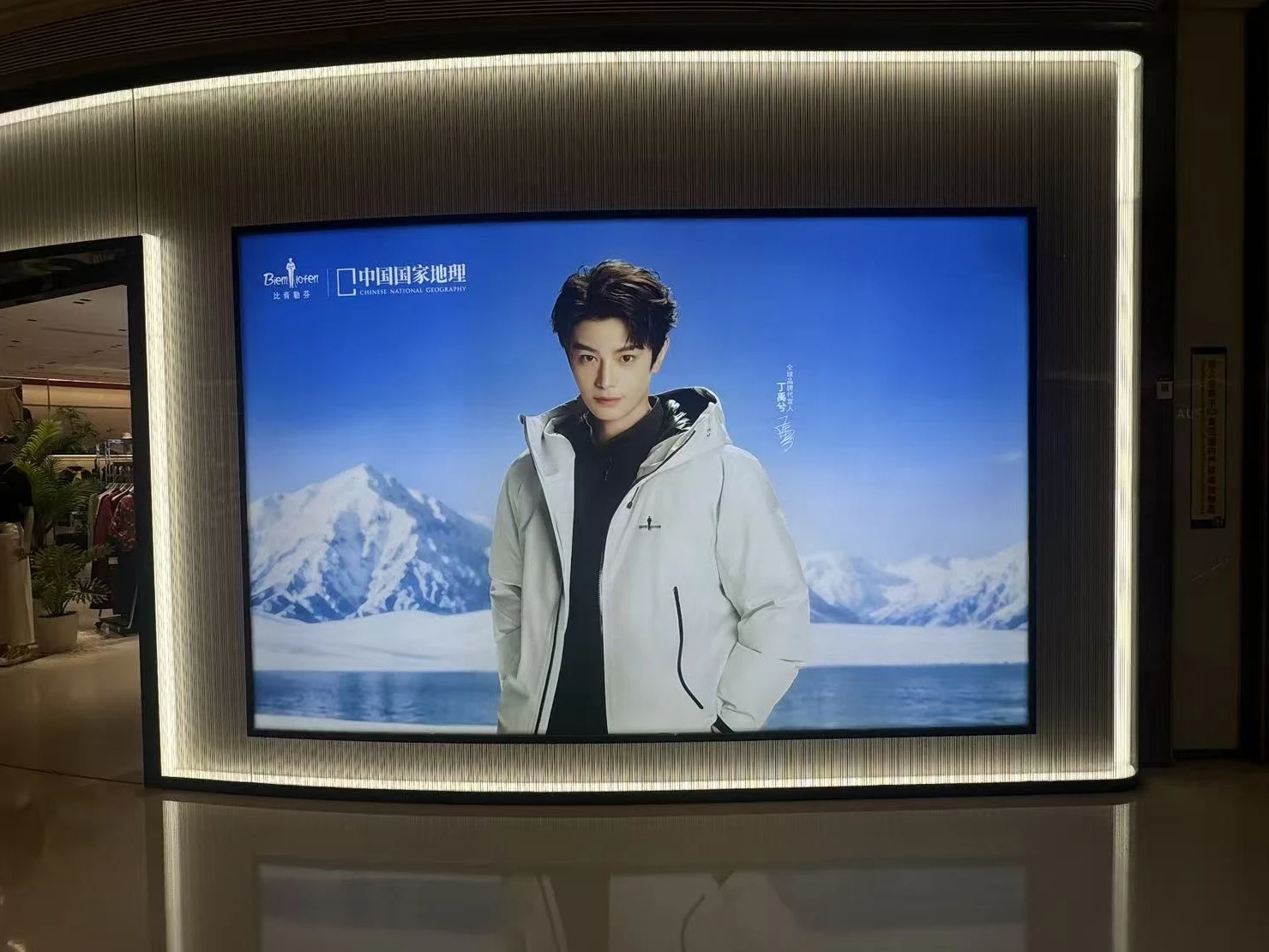 Fabric lightbox recessed into a ribbed shopfront wall, showing the Biemlofen × Chinese National Geography campaign with brand ambassador Ding Yuxi